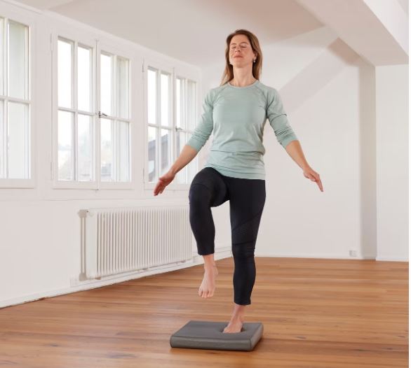 Une femme debout sur le balance pad entrain de faire un exercice de proprioception