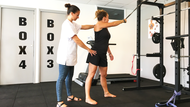 Une kiné explique à sa patiente comment tirer une sangle sur une cage de crosstraining