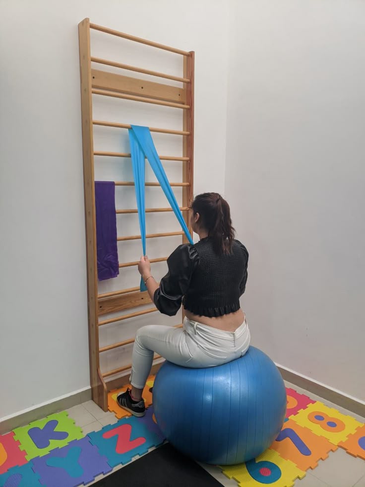 une patiente assise sur un ballon utilisant l'espalier pour un exercice de rééducation en kinésithérapie