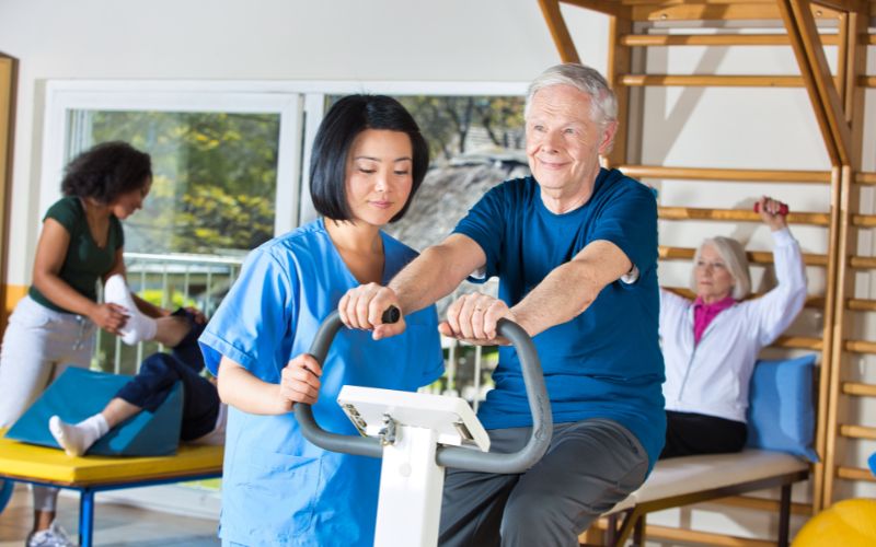 Un patient qui pédale sur un velo ergomètre avec son kiné qui lui donne des conseils pour l'usage du vélo