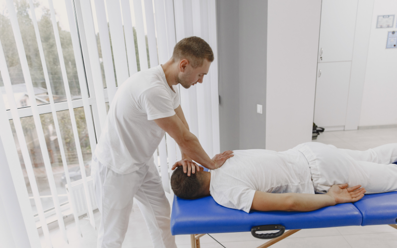 Table de massage utilisée par un kiné lors d’un soin sur un homme allongé sur le ventre