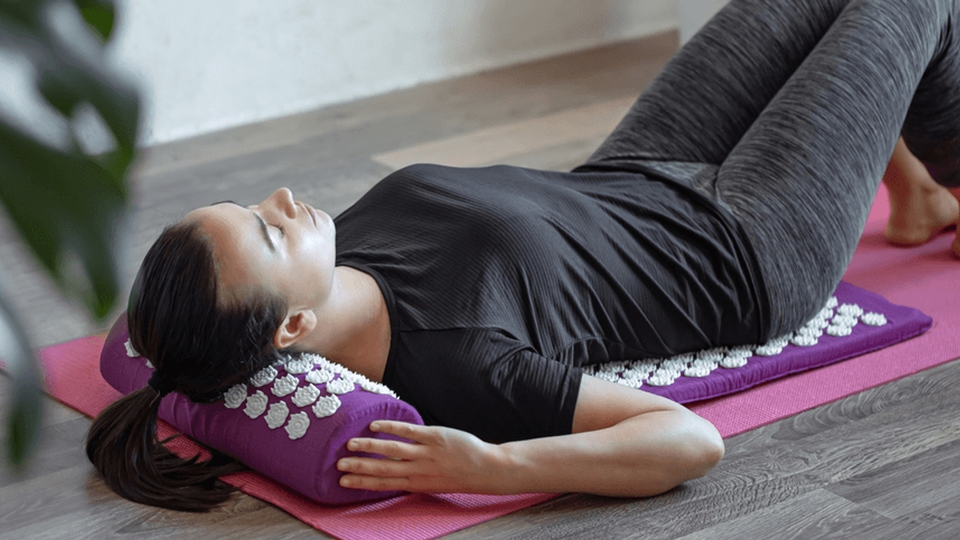 Patiente allongée sur un tapis avec un tapis d’acupression, utilisée pour la détente musculaire en kinésithérapie