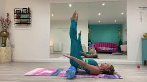 Femme allongée sur un foam roller, bras à 45°, pratiquant l'exercice The Hundred en Pilates