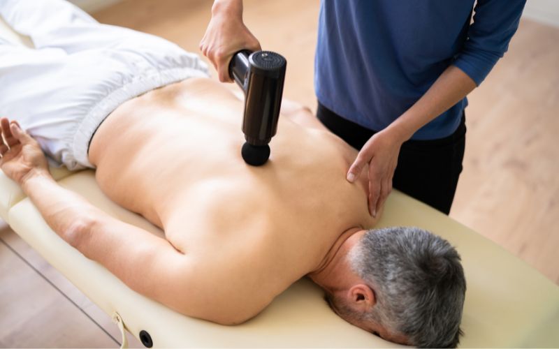 Kinésithérapeute traitant le dos d’un patient avec un pistolet de massage en séance de rééducation