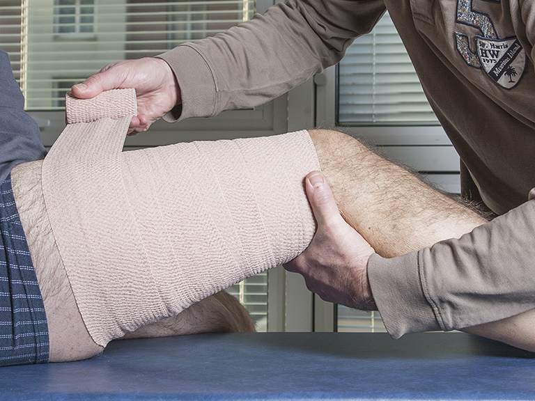 une personne qui bande une cuisse à l'aide le bande cohésive tensoplus de la gamme tensosport