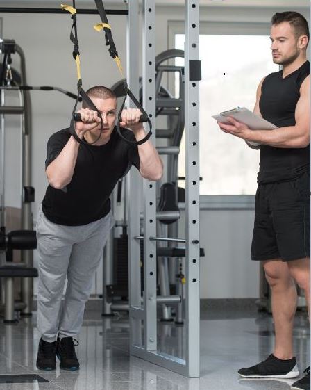 Kinésithérapeute guidant un patient lors d’un exercice de renforcement musculaire avec sangles de suspension TRX en cabinet de rééducation
